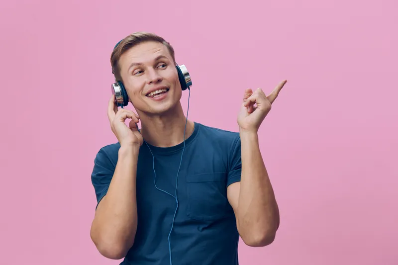 smiling man wearing headphones listen music pointing finger happy casual blue t-shirt isolated pink background digital detox mental health concept