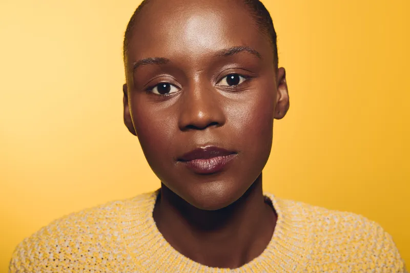 Close-up portrait of a confident African woman with dark skin wearing a yellow sweater against a yellow background. Concept of beauty, diversity, and natural skin care.