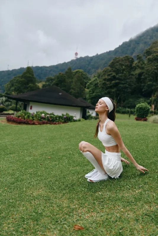 Young woman practicing yoga outdoors in a serene green landscape, wearing sporty white attire, evoking tranquility and fitness in nature
