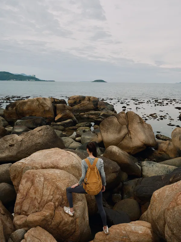 Solo female adventurer exploring rocky coastline during overcast day, showcasing determination and connection with nature