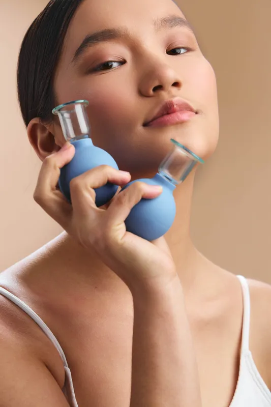 Asian woman holds blue bottles close to her face, projecting fitness focus and calm confidence in a soft studio setting, creating a serene portrait that emphasizes wellness and modern lifestyle.