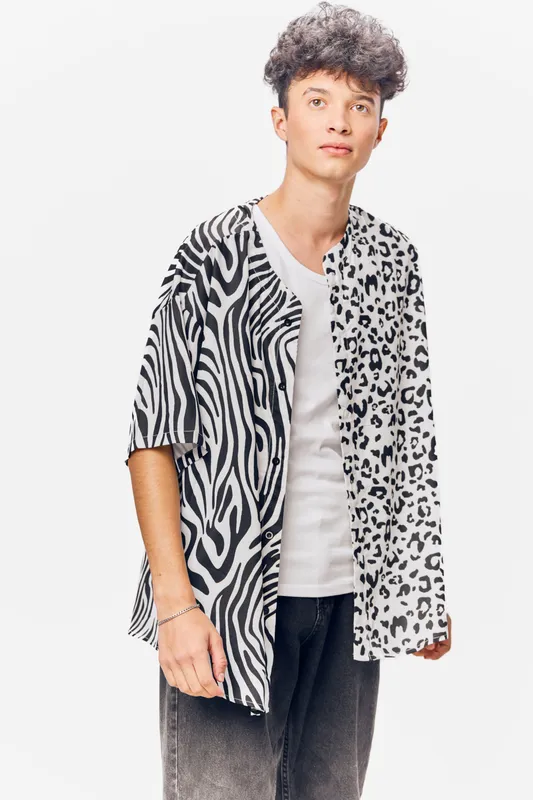 young man wearing a black and white animal print shirt and casual white t-shirt, standing against a white background with curly hair and relaxed expression