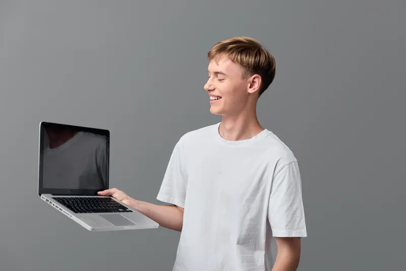 Laptop held by a smiling casual young man in a white tee, showcasing technology and digital work for remote learning, online collaboration, and product demonstration visuals