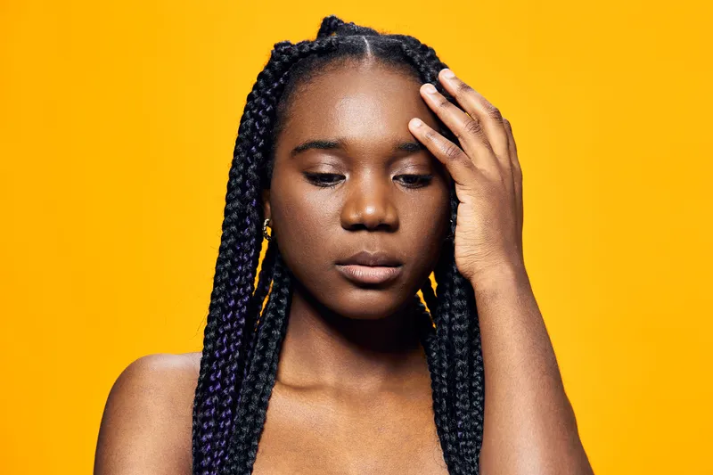Portrait of a young Black woman with braided hair, expressing contemplation against a vivid yellow background Emphasizes beauty, emotion, and strong individuality
