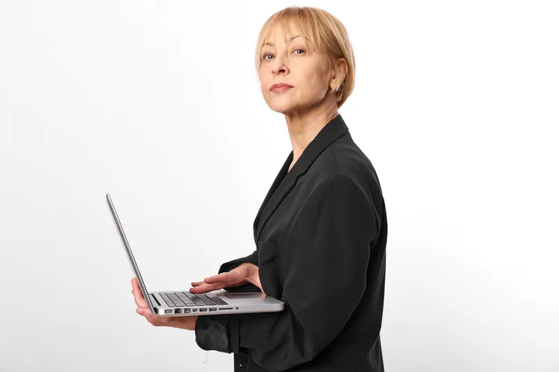 Businesswoman in office attire typing on a laptop in a studio, white background, side portrait. Professional expression and computer work suggest productivity, communication, and focused remote