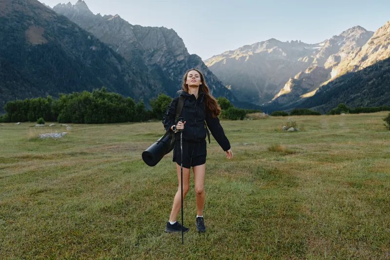 A solo photographer stands in a wide alpine meadow with a camera and tripod, set against rugged mountains, conveying focus, adventure, and creative energy.