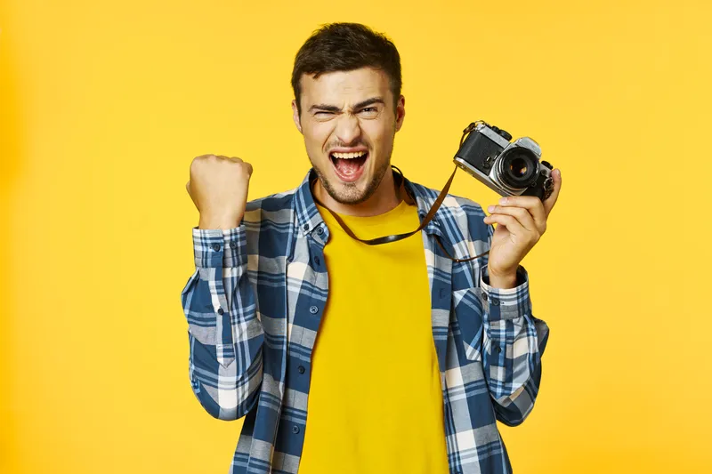 Успешный мужчина в жёлтой футболке с фотоаппаратом в руке испытывает радость