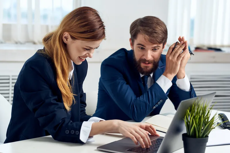 Коллеги работают вместе за ноутбуком в офисе, используя современные технологии