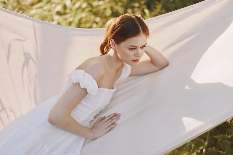 Young woman in white dress resting on a hammock, showcasing tranquility in nature, featuring soft colors and a serene atmosphere