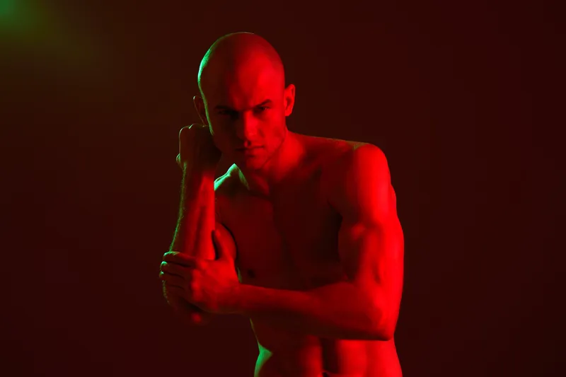 Athletic man posing confidently in dramatic red lighting, emphasizing strength and determination, creating a striking visual impact in a bold atmosphere.