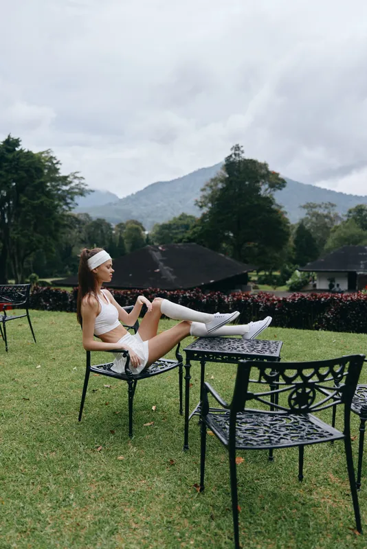 Young woman in sportswear enjoying a moment of relaxation outdoors, surrounded by greenery and mountains, embodying a healthy lifestyle and fitness concept