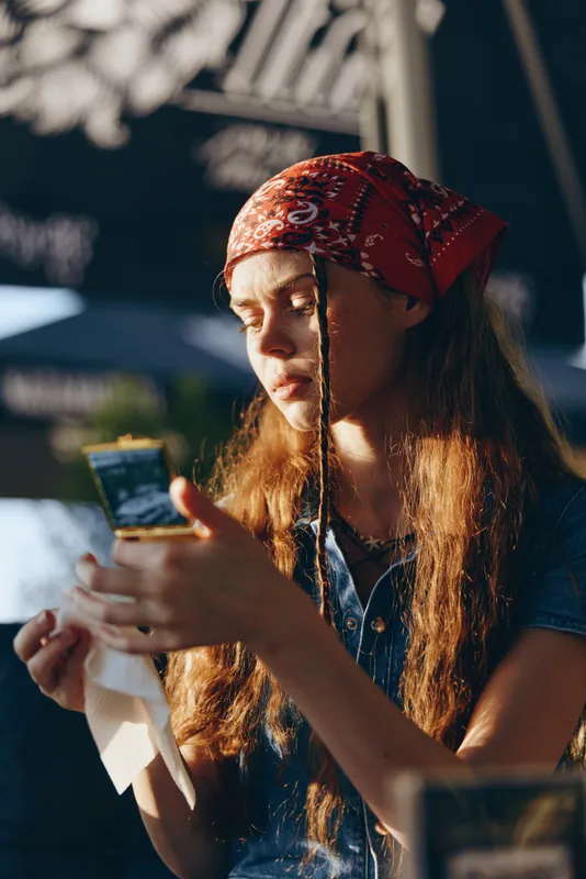 lifestyle woman in modern boho-western denim street style with bandana, warm natural light, film color tones, casual and thoughtful mood outdoors