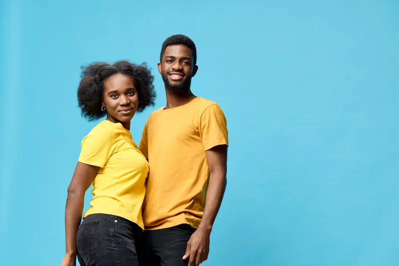 A cheerful young African couple in matching yellow shirts against a vibrant blue background, showcasing happiness and connection in a bright, modern setting