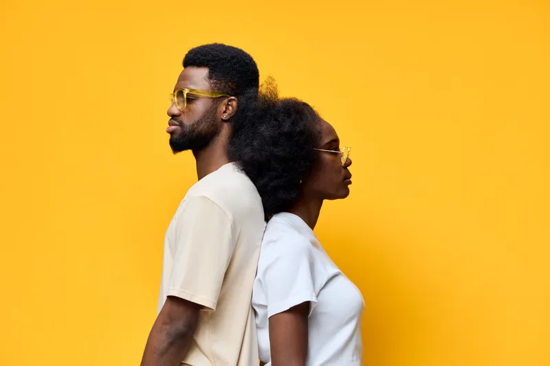 Young African couple in stylish casual outfits against a vibrant yellow background, showcasing love and connection through body language and emotion