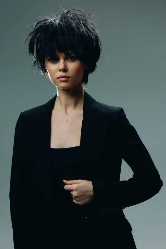 stylish woman with short black hair wearing modern black blazer posing against dark background