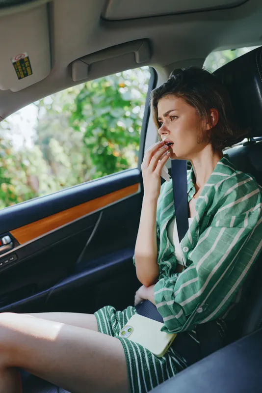A contemplative person sits in a car, wearing a green striped shirt, gazing ahead with a thoughtful expression.