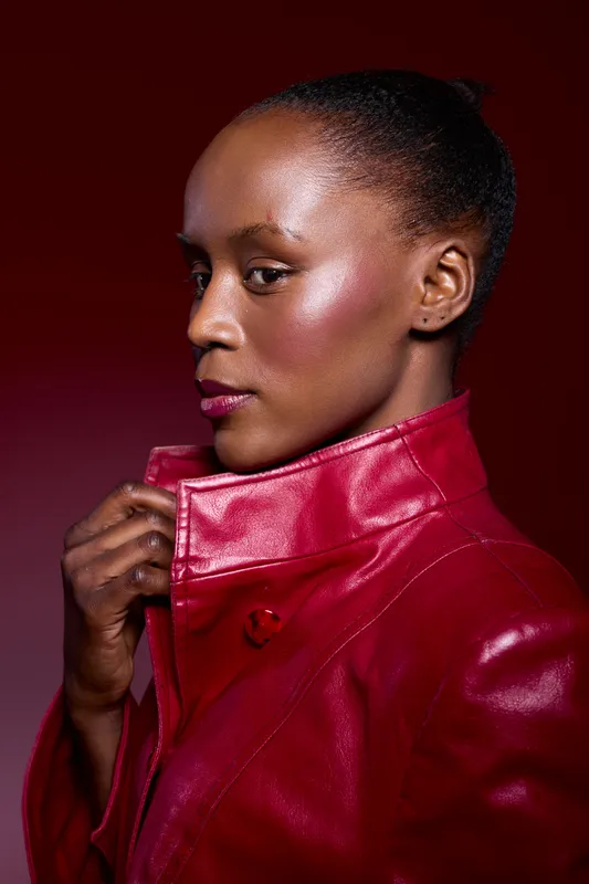 Portrait of a dark skinned African woman wearing a red leather jacket against a red gradient background. She looks confident and stylish with natural makeup and braided hair. Fashion concept.