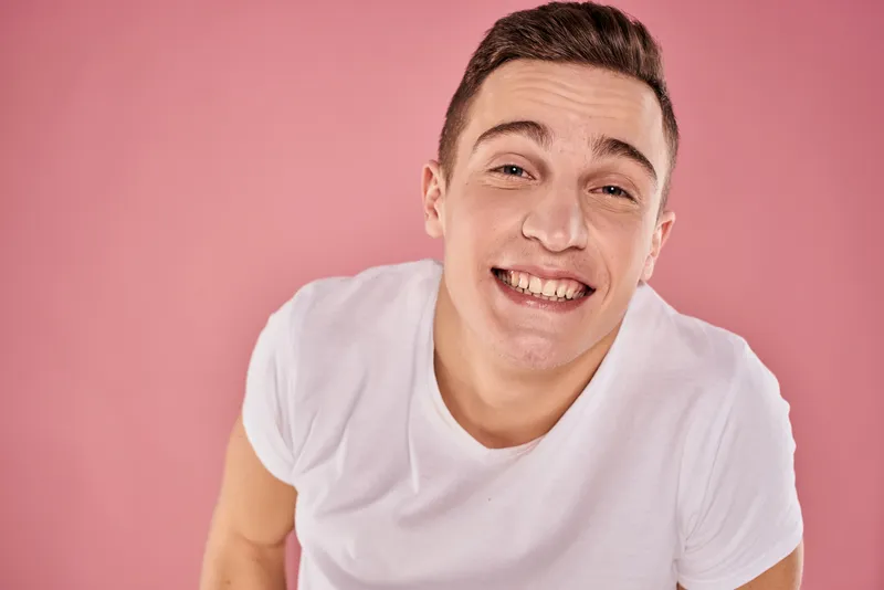 Весёлый мужчина в белой футболке улыбается, крупный план, розовый фон, студия