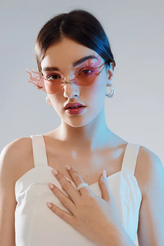 Young woman beauty fashion portrait wearing unique pink sunglasses and white top. Studio shot with soft lighting highlights her flawless skin and stylish look. Concept of modern style.