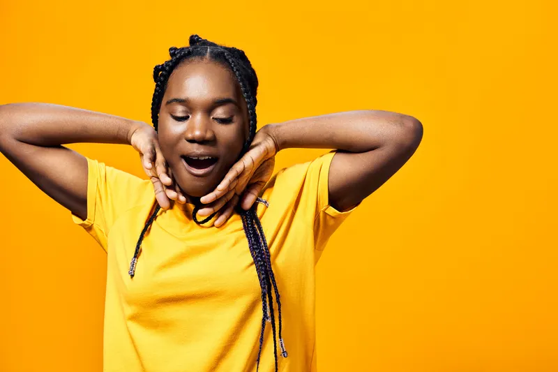 Happy young Black woman in a bright yellow t shirt expressing joy and relaxation against a vibrant yellow background