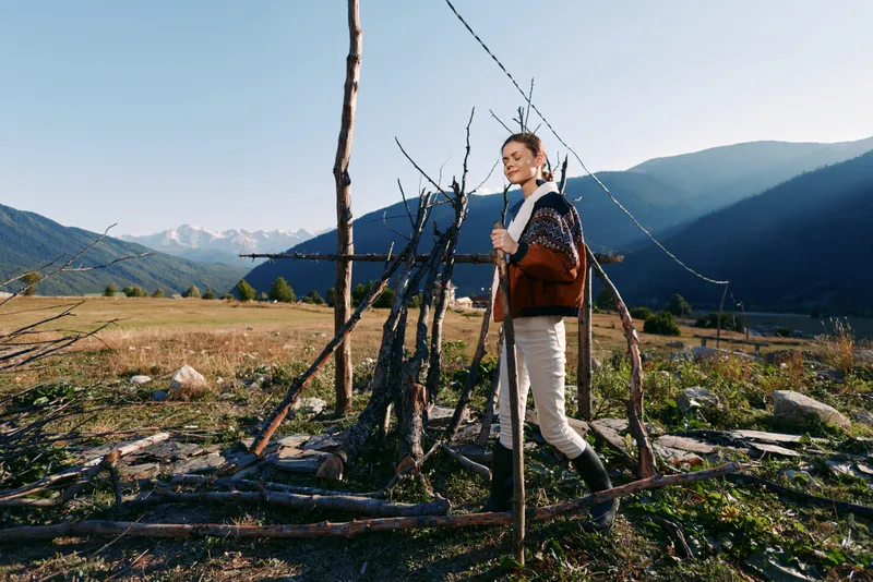 Woman hiker in mountains with backpack and walking stick in meadow, enjoying nature and scenic trail. Outdoor travel and hiking adventure with sunlight and peaceful rural landscape.