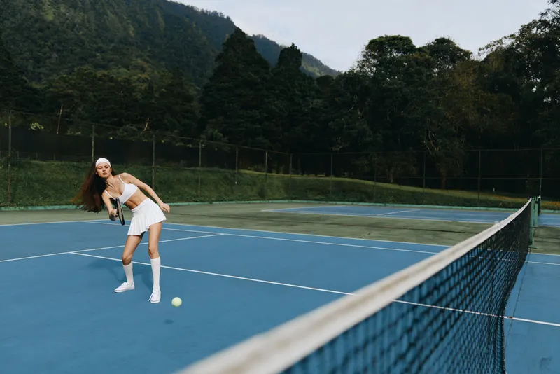 Young female athlete playing tennis on a blue court, showcasing determination and energy while wearing sporty attire with a vibrant background