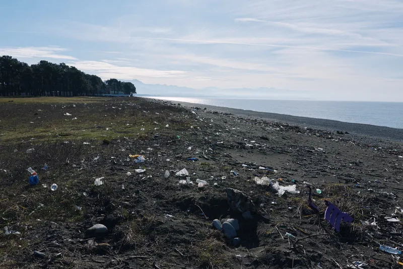 Beach scene with litter and debris along the coastline, polluted shore and water highlighting environmental impact of waste on ocean life and habitat