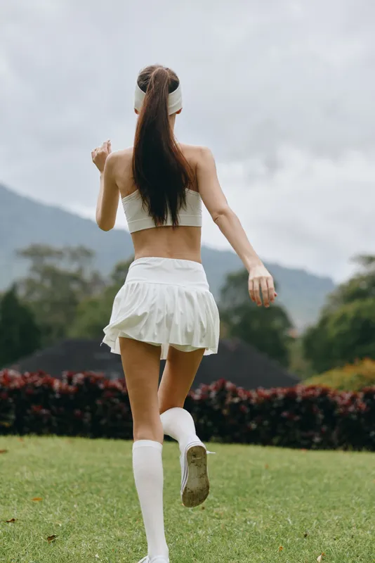 Young athletic woman in white sports outfit running on green grass in a vibrant landscape, embodying fitness, health, and motivation in a seasonal outdoor setting