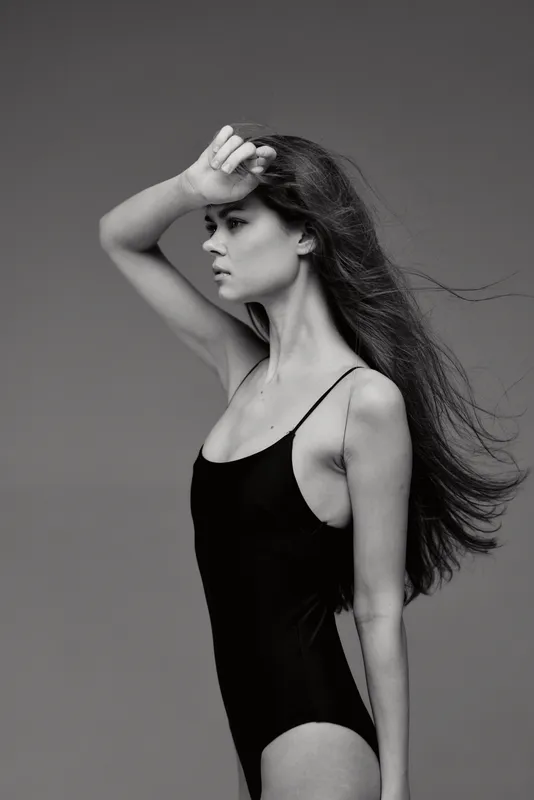 Black and white portrait of a woman in a black bodysuit with windblown hair and thoughtful expression