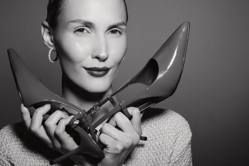 Portrait of a fair skinned Caucasian woman holding two high heel shoes close to her face with confident expression in studio.