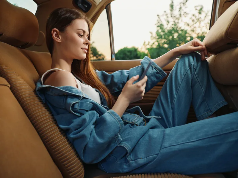 Young woman in denim outfit relaxing in the backseat of a car, enjoying a moment of calm and tranquility, showcasing modern lifestyle and comfort.