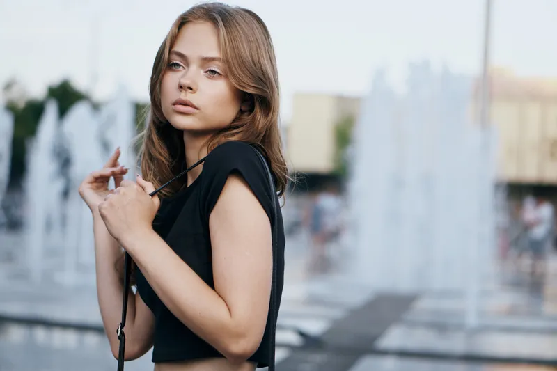 Женщина у фонтана на улице в чёрной футболке, кадр обрезан, распущенные волосы, красивая модель