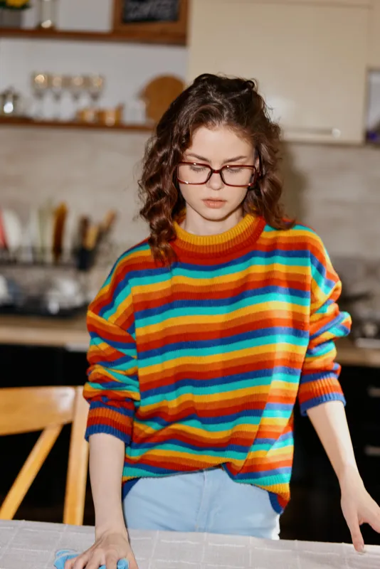 Young woman with curly hair and glasses stands in a bright kitchen, wearing a colorful striped sweater. Close up on her hands and everyday tasks, highlighting home life and cozy comfort in a warm