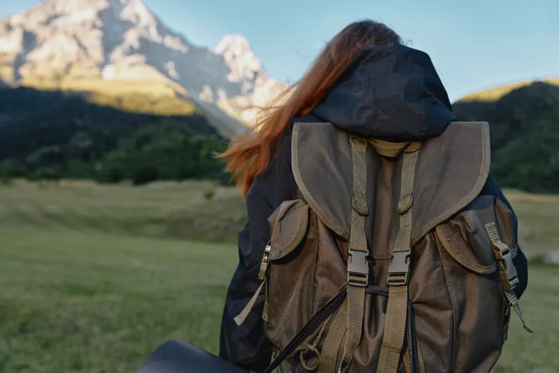 A traveler stands in a scenic alpine landscape wearing a rugged backpack and outdoor gear. The vast mountain backdrop and fresh air convey adventure, exploration, and freedom.