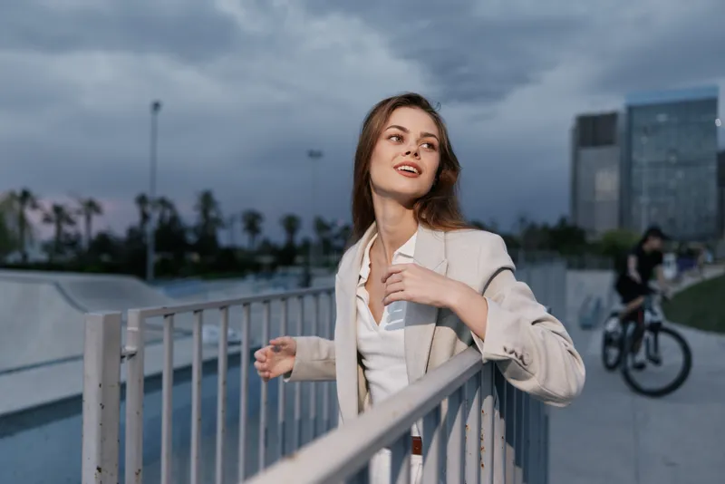 confident woman in beige jacket outdoors during evening cityscape with urban background and relaxed joyful expression