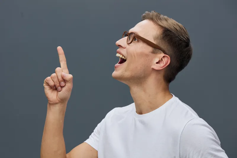 smiling caucasian man wearing glasses white t-shirt pointing side isolated on gray background digital content generation concept