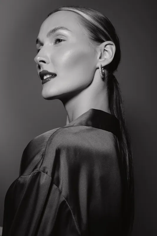 Elegant white woman with pale skin and dark lipstick poses in satin outfit in studio. Concept of fashion, beauty, and glamour in black and white photography.