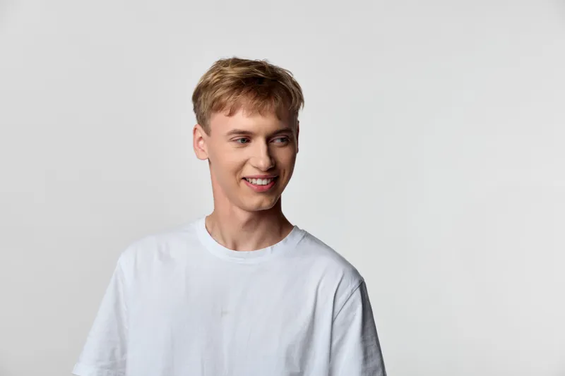 Smiling man in a white tee stands against a clean studio background, showcasing casual fashion, a relaxed posture, and a friendly mood suitable for lifestyle, advertising, or ecommerce branding