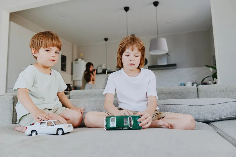 Two children playing with toy cars in a cozy living room, showcasing a joyful and playful atmosphere. Perfect for family-oriented themes.
