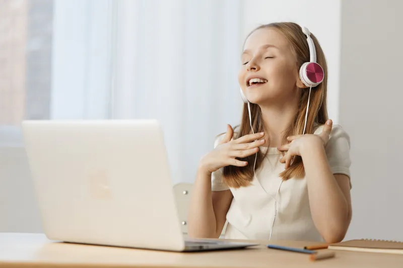 Young girl enjoying music with headphones while sitting at a laptop, expressing happiness and joy Bright indoor setting with soft natural light