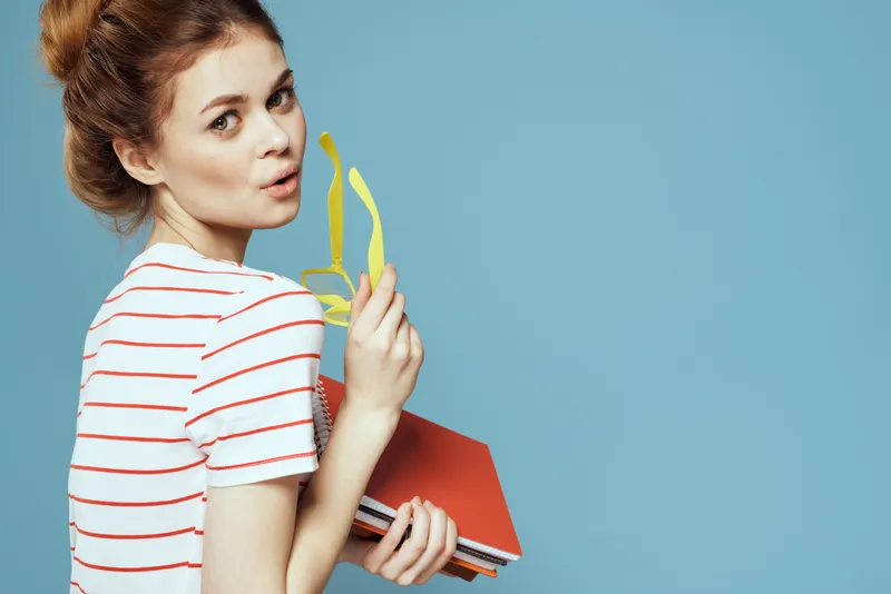Красивая студентка с блокнотами и в жёлтых очках на синем фоне
