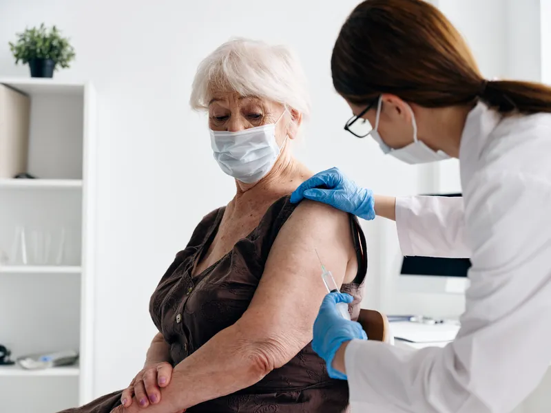 Медсестра рядом с пациентом делает инъекцию вакцины в больнице, используя паспорт вакцинации