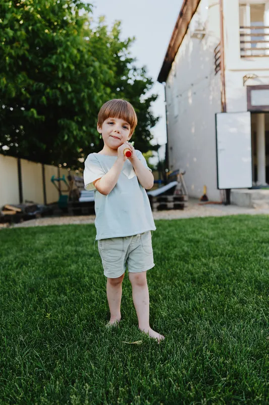 Playful boy enjoying summer outdoors, holding a toy in a green garden. The image captures joyful moments of childhood and sunny weather in a vibrant setting.
