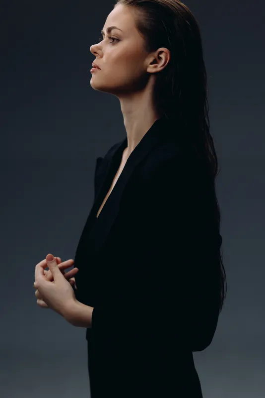 serious woman in black jacket with long hair standing against dark background in thoughtful pose