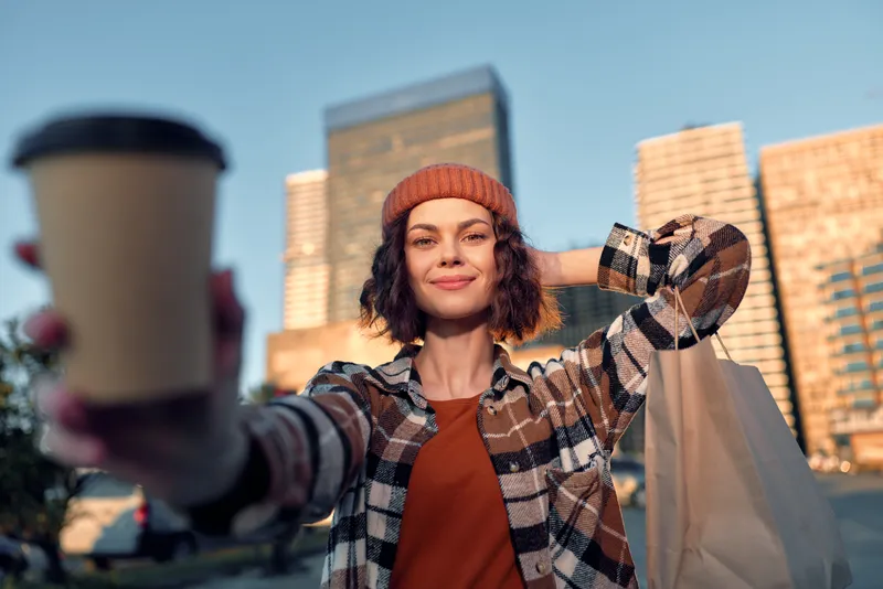 Woman holding coffee and shopping bag in city urban portrait, smile and candid lifestyle captured in golden hour glow, authenticity, mindful living and emotional storytelling in warm light.