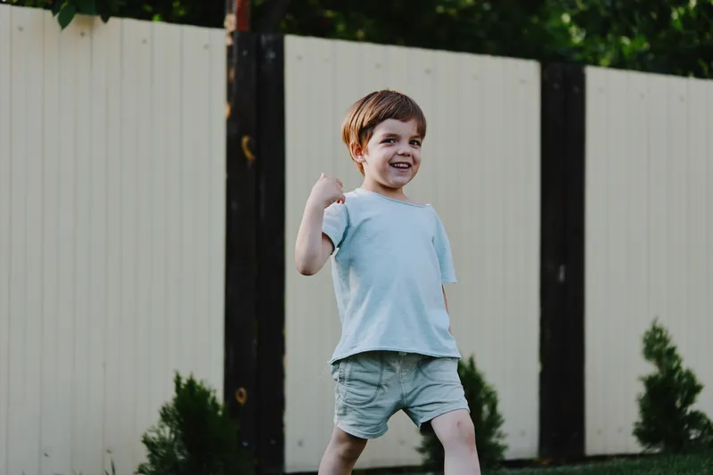 Joyful boy walking outdoors with a smile, dressed casually in light clothes, surrounded by greenery and a serene environment perfect for outdoor activities.