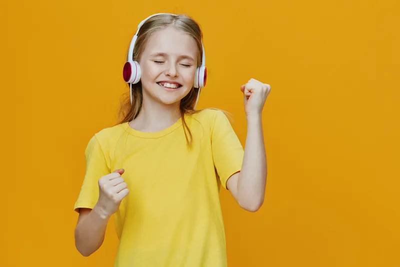 Happy girl dancing in a yellow shirt and headphones against a bright yellow background, expressing joy and music enjoyment
