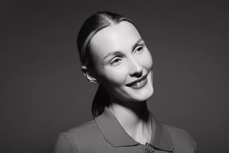 Smiling white woman with pale skin and brown hair wears vintage clothing on dark background. Portrait in black and white lighting.