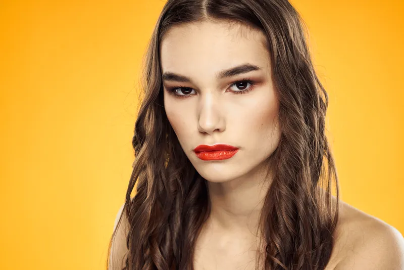 Женщина с обнажёнными плечами, красными губами и очаровательной улыбкой на жёлтом фоне