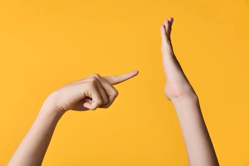 Hands forming a pointing gesture toward a raised hand on a bright yellow background, a clear cue for attention, interaction and focus in a clean studio setup